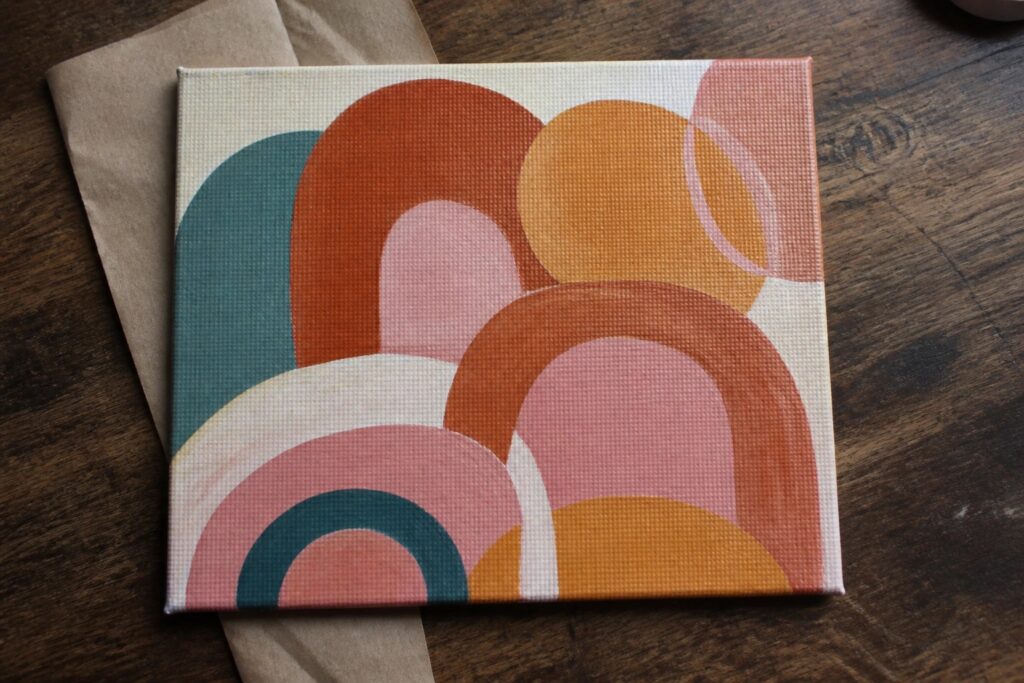Abstract canvas with overlapping colorful semicircles in teal, orange, peach, and yellow on wood