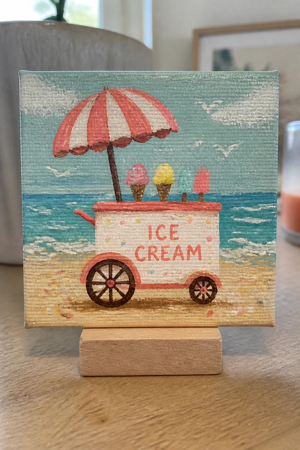 Miniature canvas painting of an ice cream cart with striped umbrella on the beach.