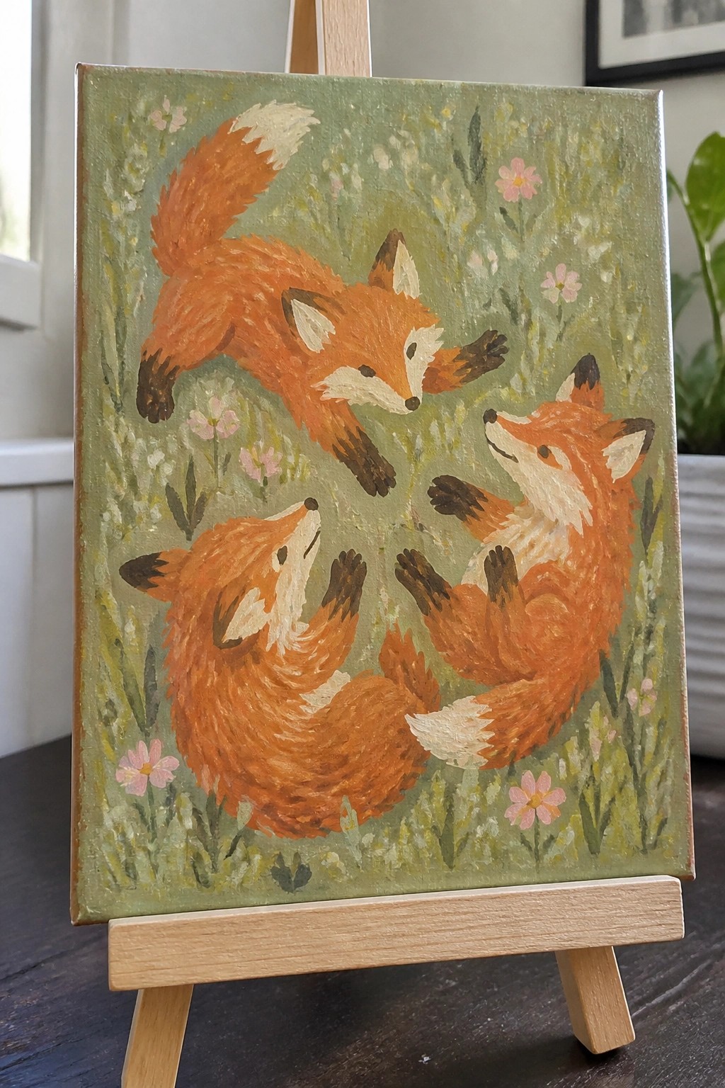 Three orange foxes playing in a green meadow with pink flowers, on wooden easel