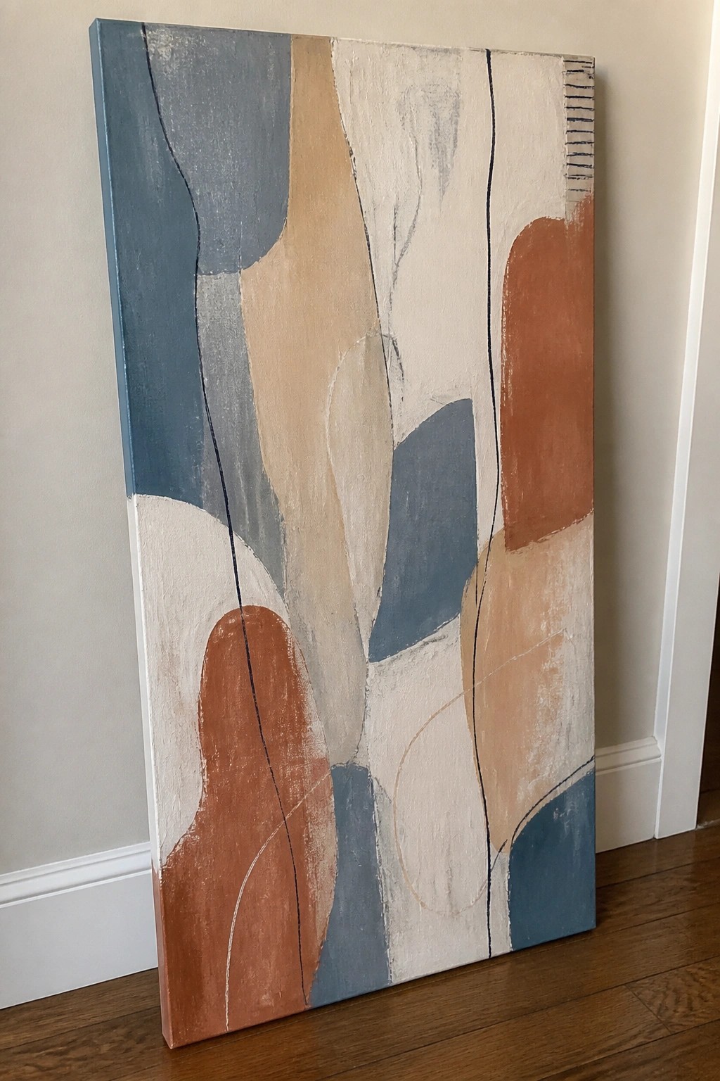 Abstract canvas painting with organic blue, beige, and terracotta shapes leaning on wooden floor.