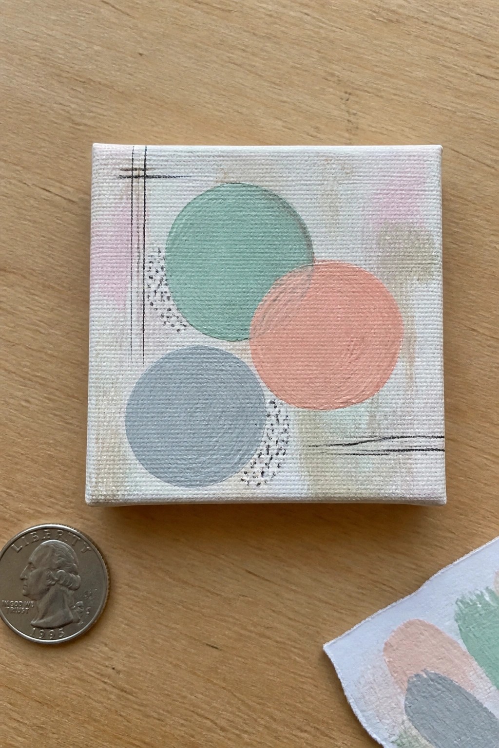 Mini canvas with overlapping green, coral, and gray circles beside a quarter on wood.