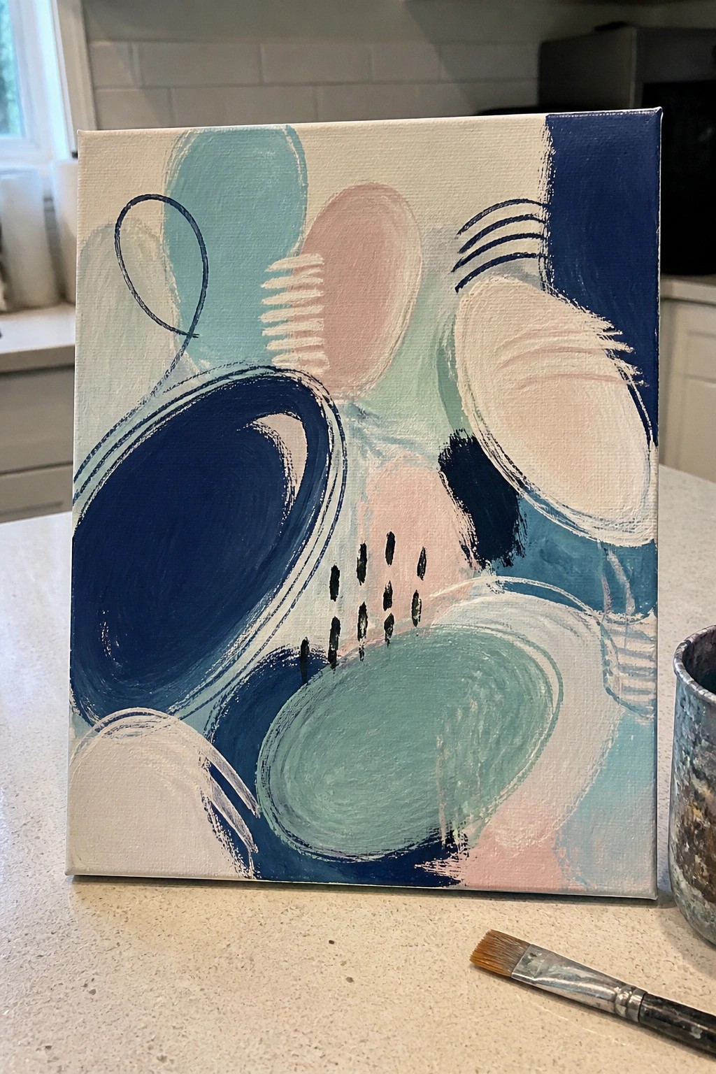 Abstract painting with navy blue, teal, and pink shapes on kitchen countertop