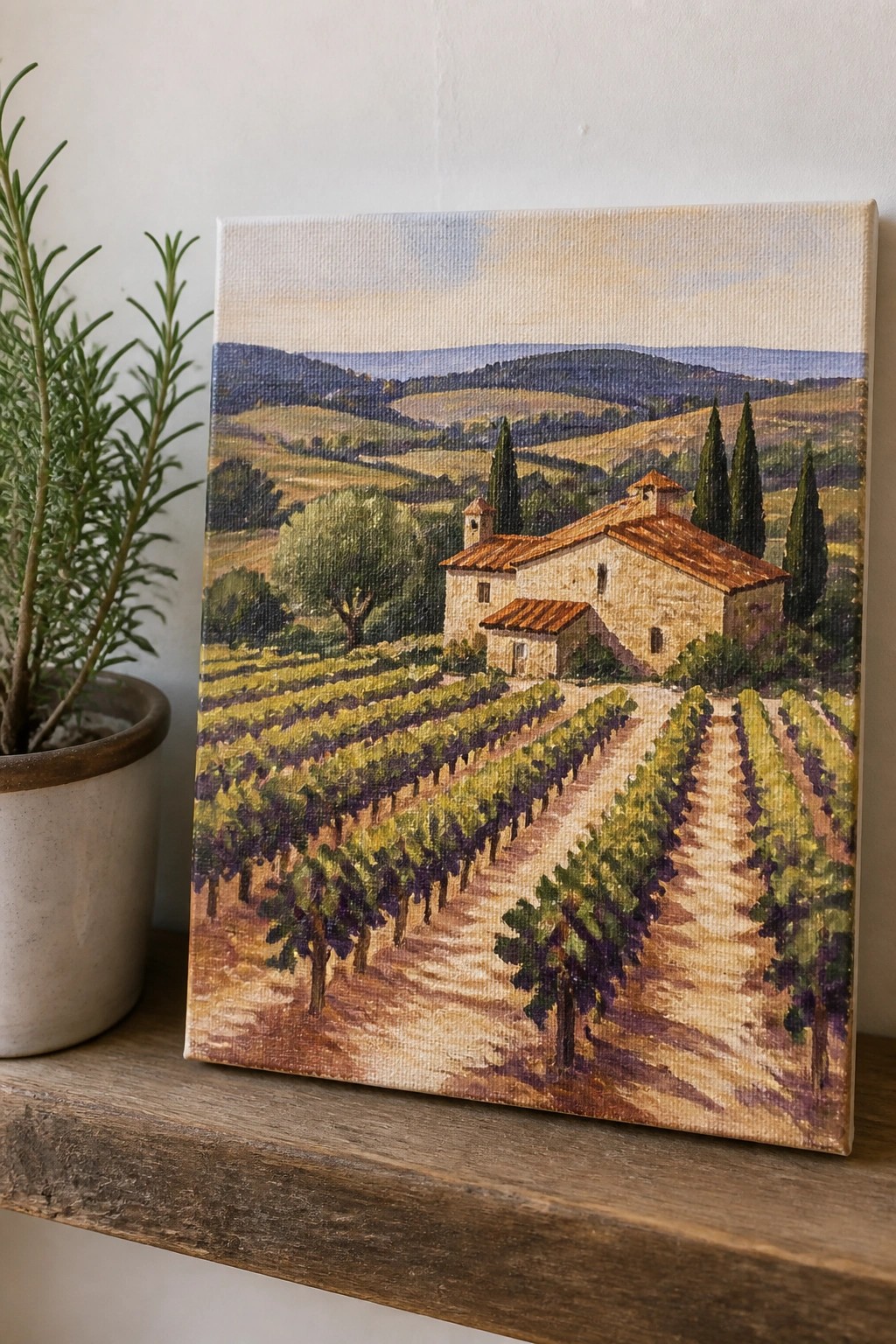 Painting of vineyard with stone house, cypress trees beside potted plant on wooden shelf