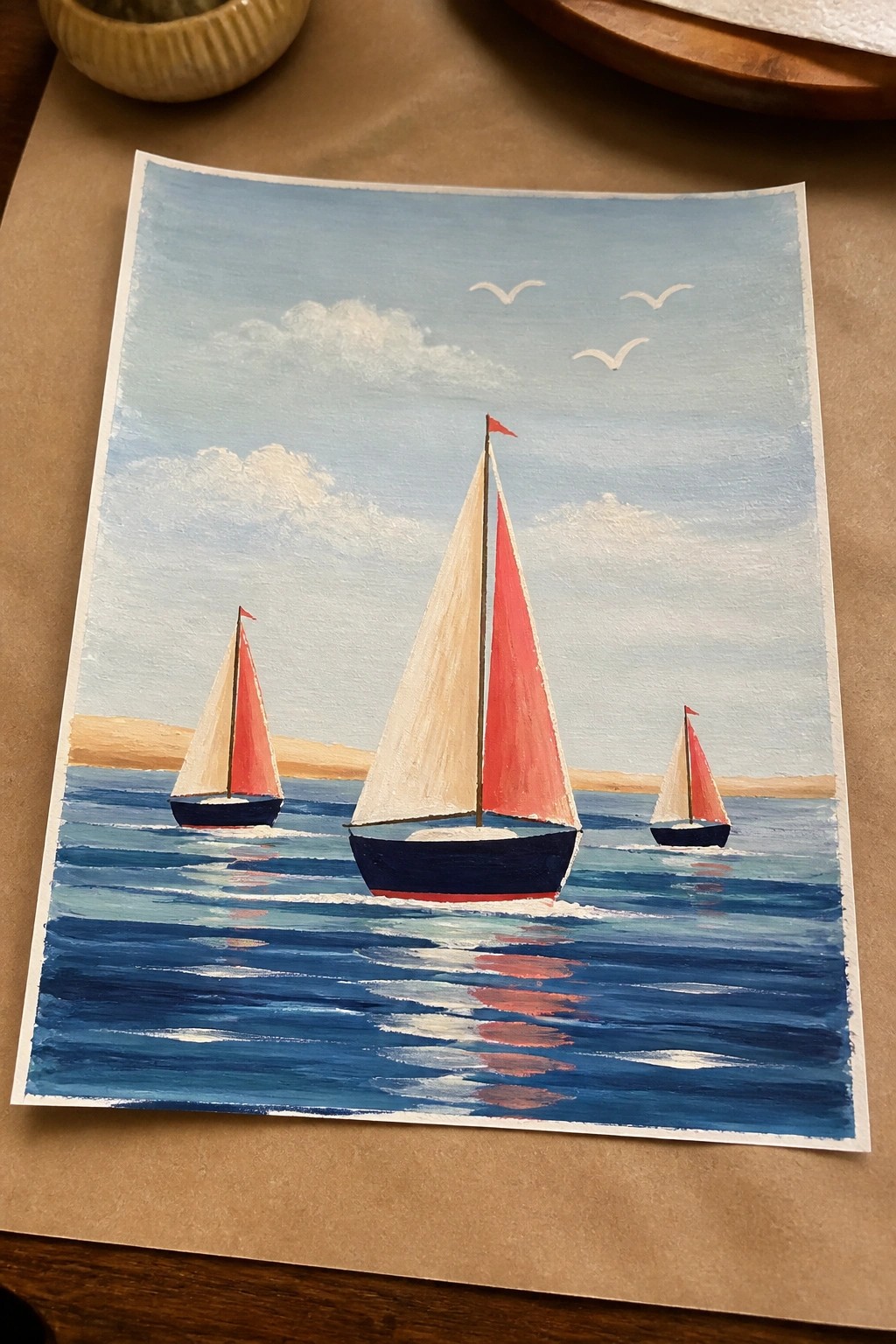 Three sailboats with red sails on blue water under cloudy sky with birds