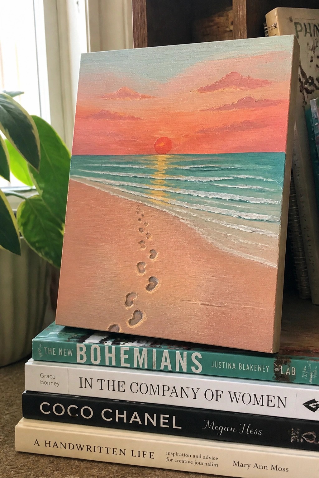 Beach sunset painting with footprints propped on stack of books