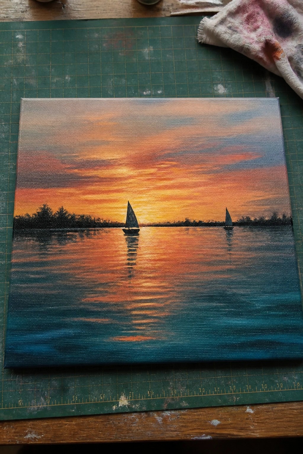 Silhouetted sailboats on reflective water under vibrant orange-blue sunset sky on canvas.