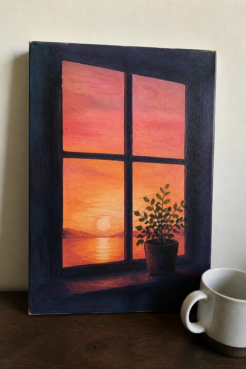 Canvas painting of orange sunset through dark blue window with potted plant and white mug.
