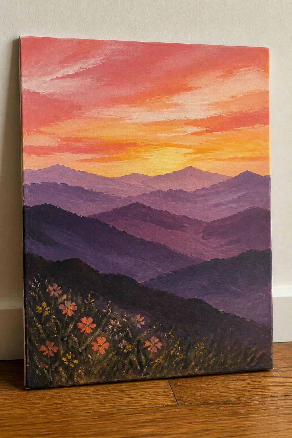 Layered purple mountains beneath vibrant red-orange sunset sky with foreground wildflowers.