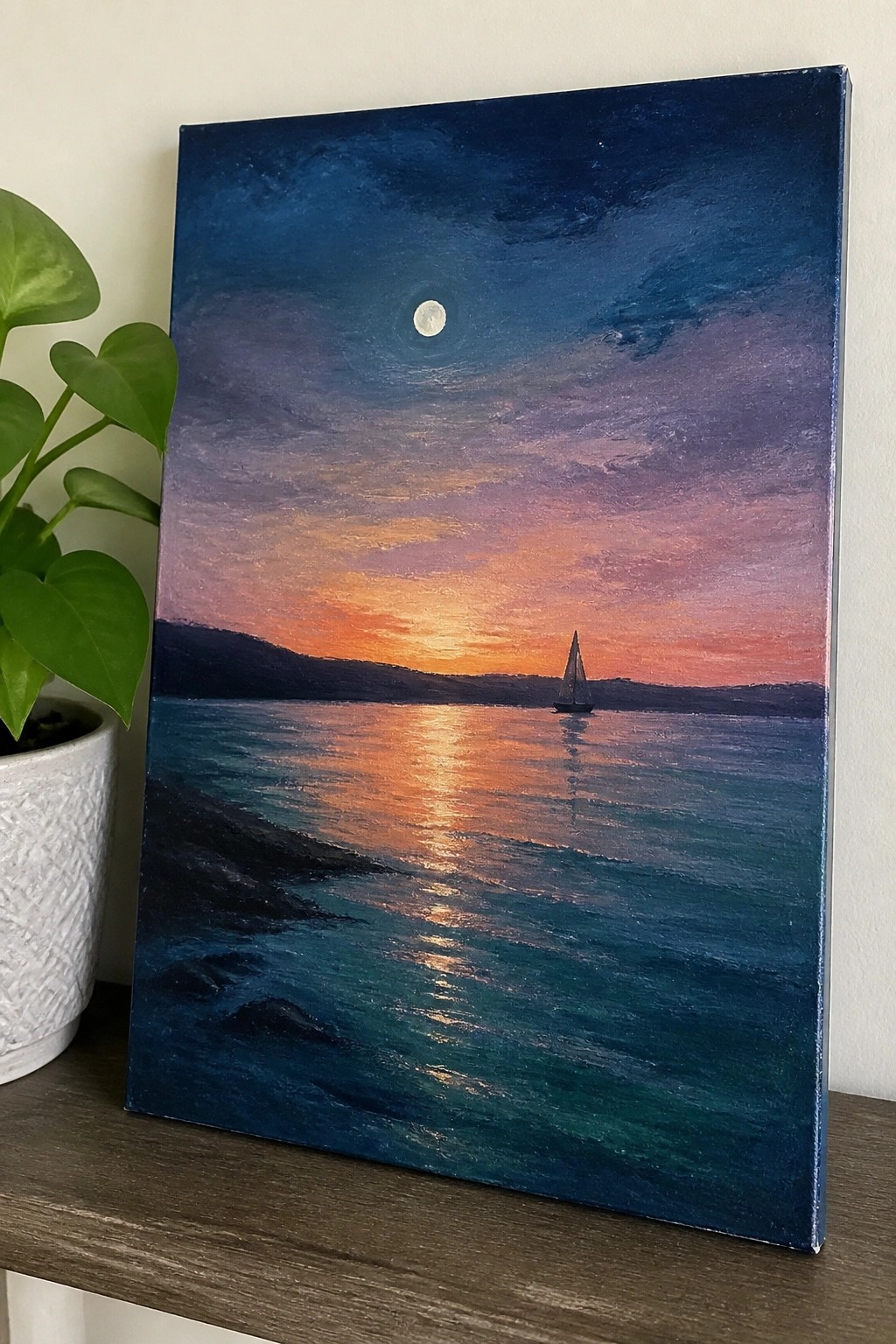 Painting of sailboat on colorful sunset ocean with moon above, plant beside it.