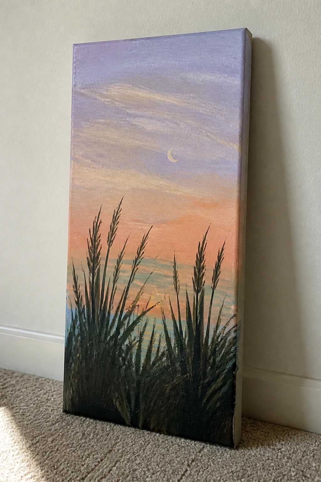Tall reeds frame a sunset seascape with crescent moon on leaning canvas.