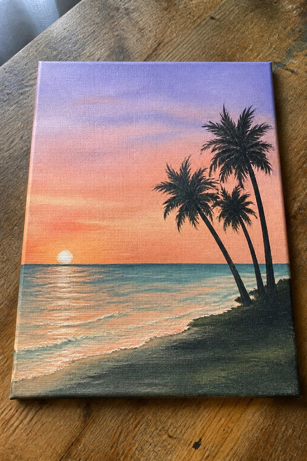 Canvas painting of ocean sunset with orange-pink sky and three silhouetted palm trees.