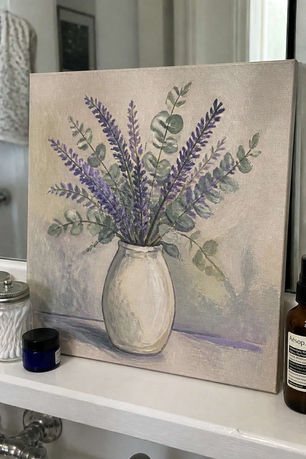 Floral painting of purple lavender and eucalyptus in white vase on bathroom counter