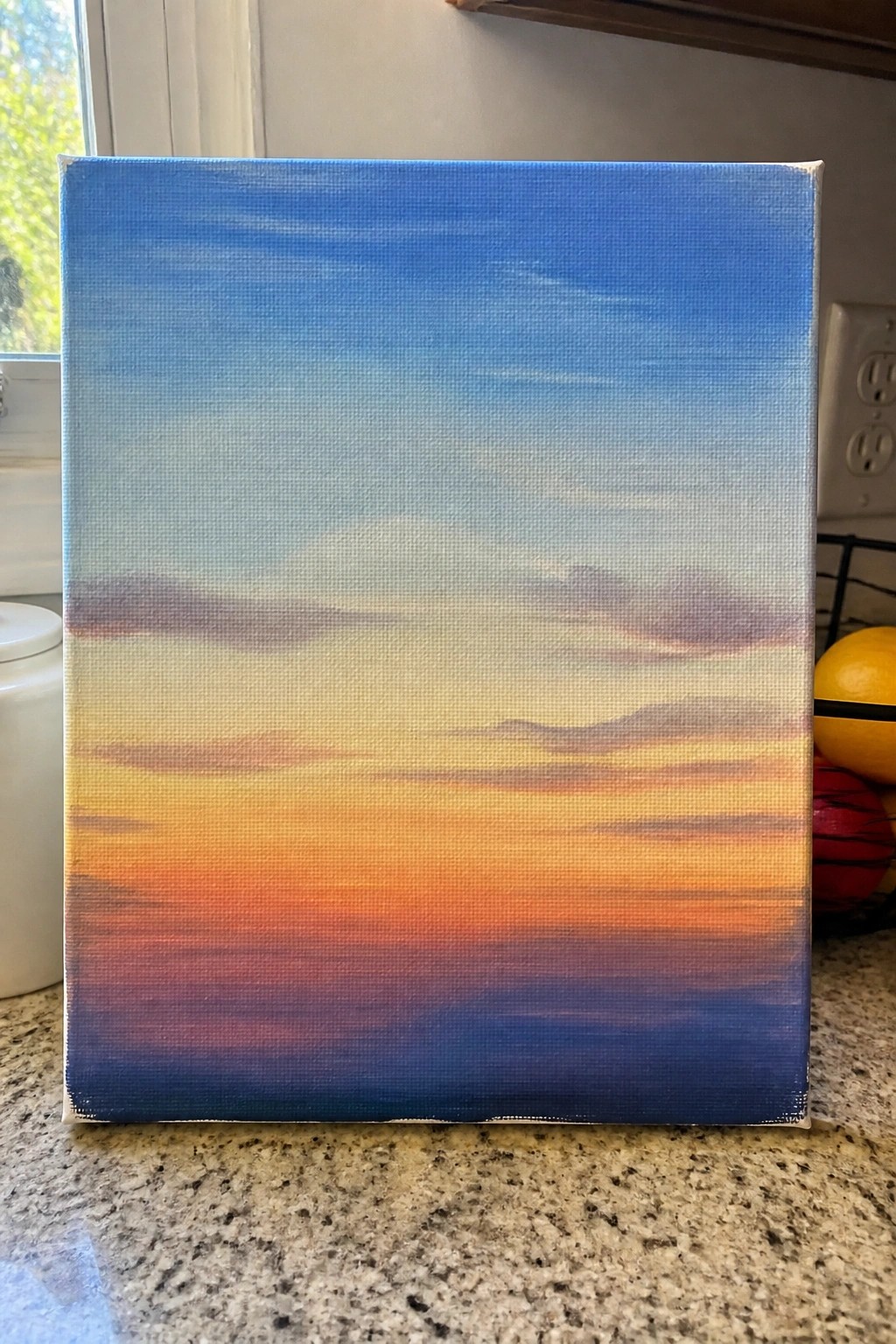 Canvas painting of blue-to-orange sunset gradient with distant hills on granite counter