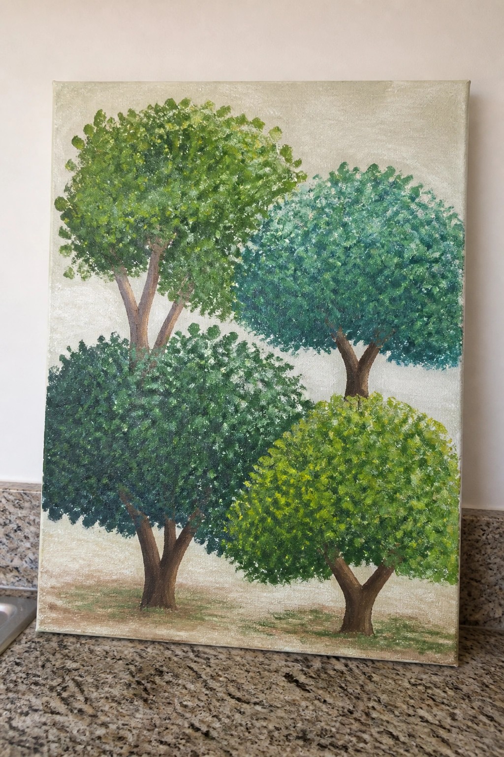 Painting of four green trees on canvas atop speckled countertop