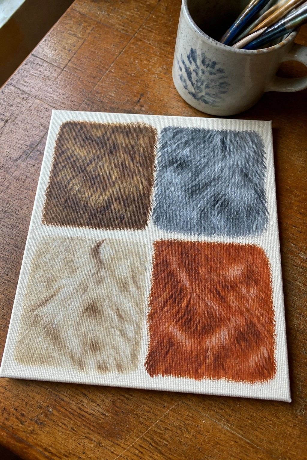 Canvas with four colored fur textures beside a mug of brushes on wood