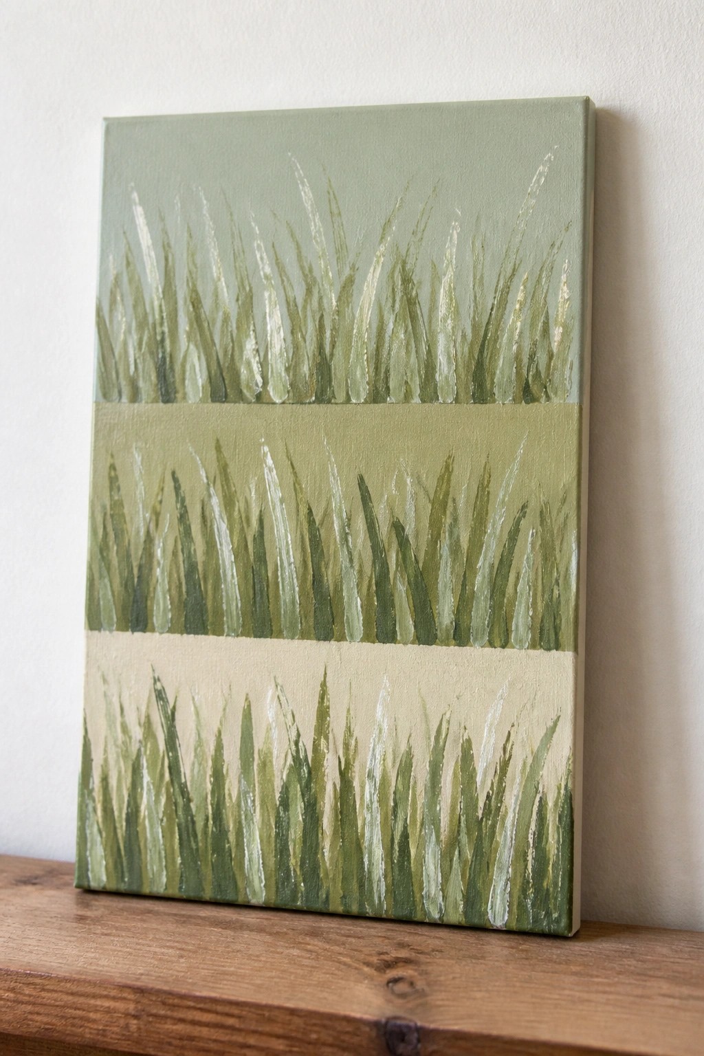 Rectangular canvas with green grass strokes on wooden surface against white wall
