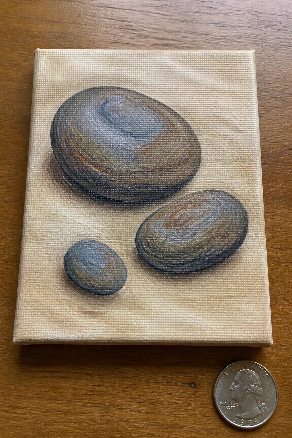 Small canvas painting of three gray-brown stones beside a 1994 quarter on wood
