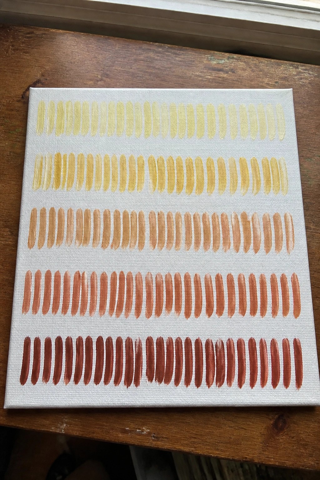 Canvas with rows of oval shapes in yellow-to-red gradient on wooden surface.