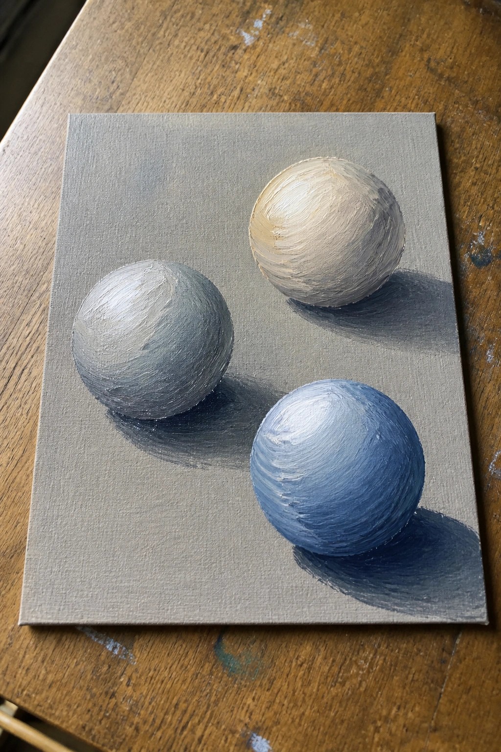 Three spheres in gray, blue, and beige with soft shadows on gray canvas.