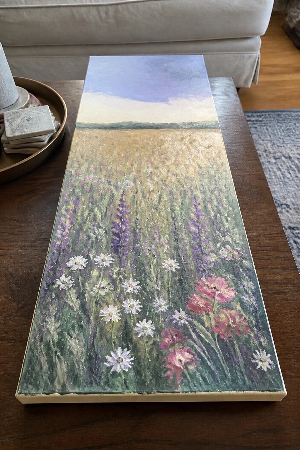 Wildflower meadow painting with white daisies, pink and purple blooms on wooden table.
