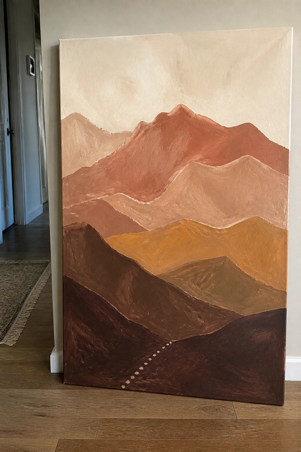 Layered mountain painting in earthy browns and oranges leaning on hardwood floor.