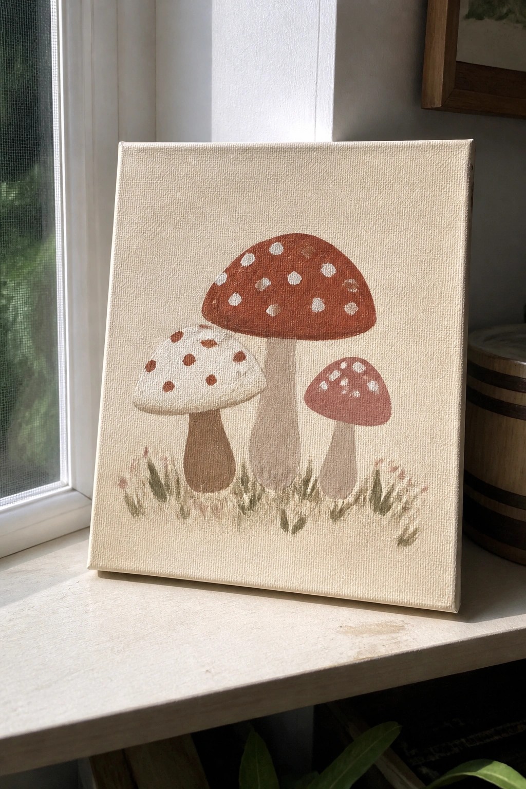 Painting of three mushrooms with red spotted caps on grass beside window