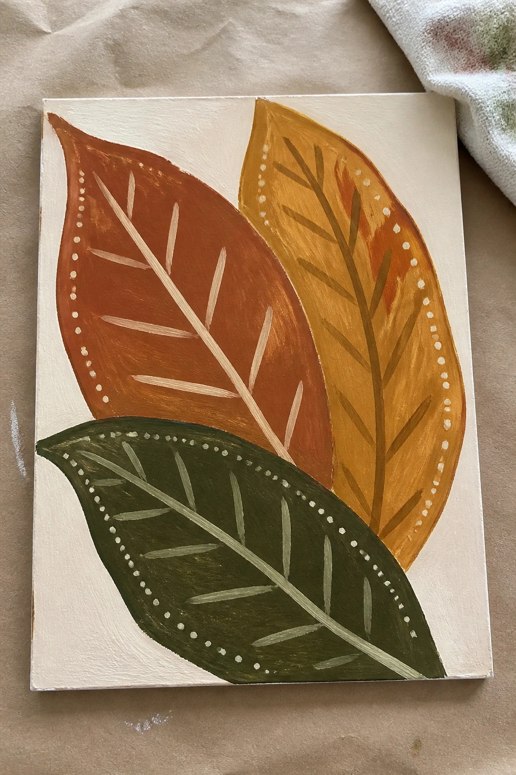 Abstract painting of three overlapping leaves in red, yellow, and green on canvas