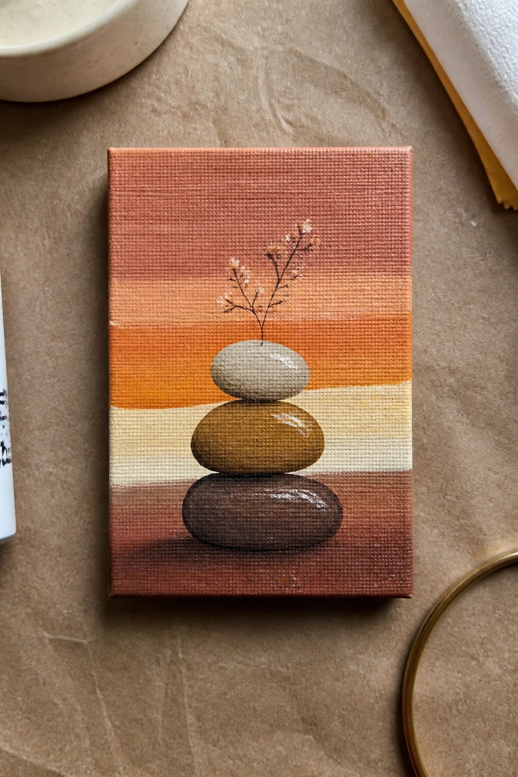 Stacked pebbles with delicate sprig atop, painted on canvas in warm orange stripes