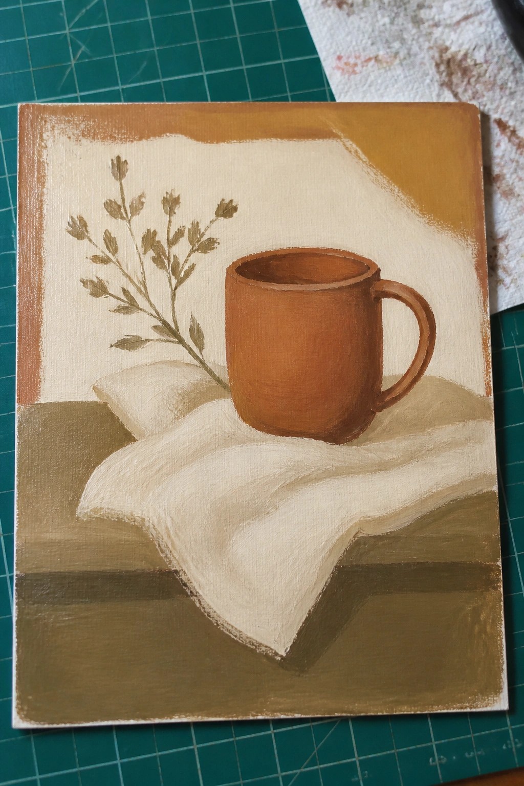 Still life of brown mug on white cloth beside dried plant in earthy tones