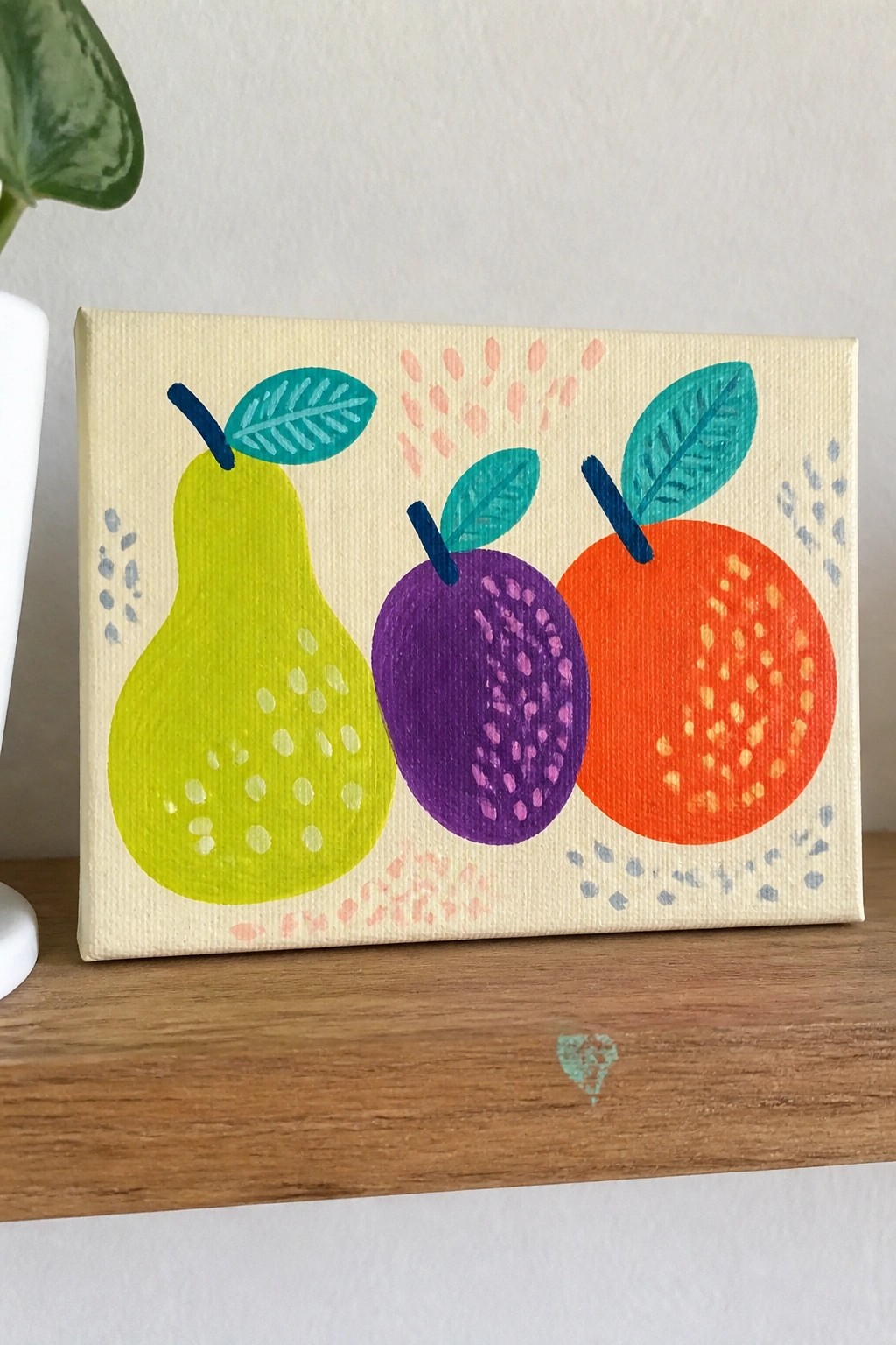 Colorful painting of green pear, purple plum, and orange with teal leaves on canvas