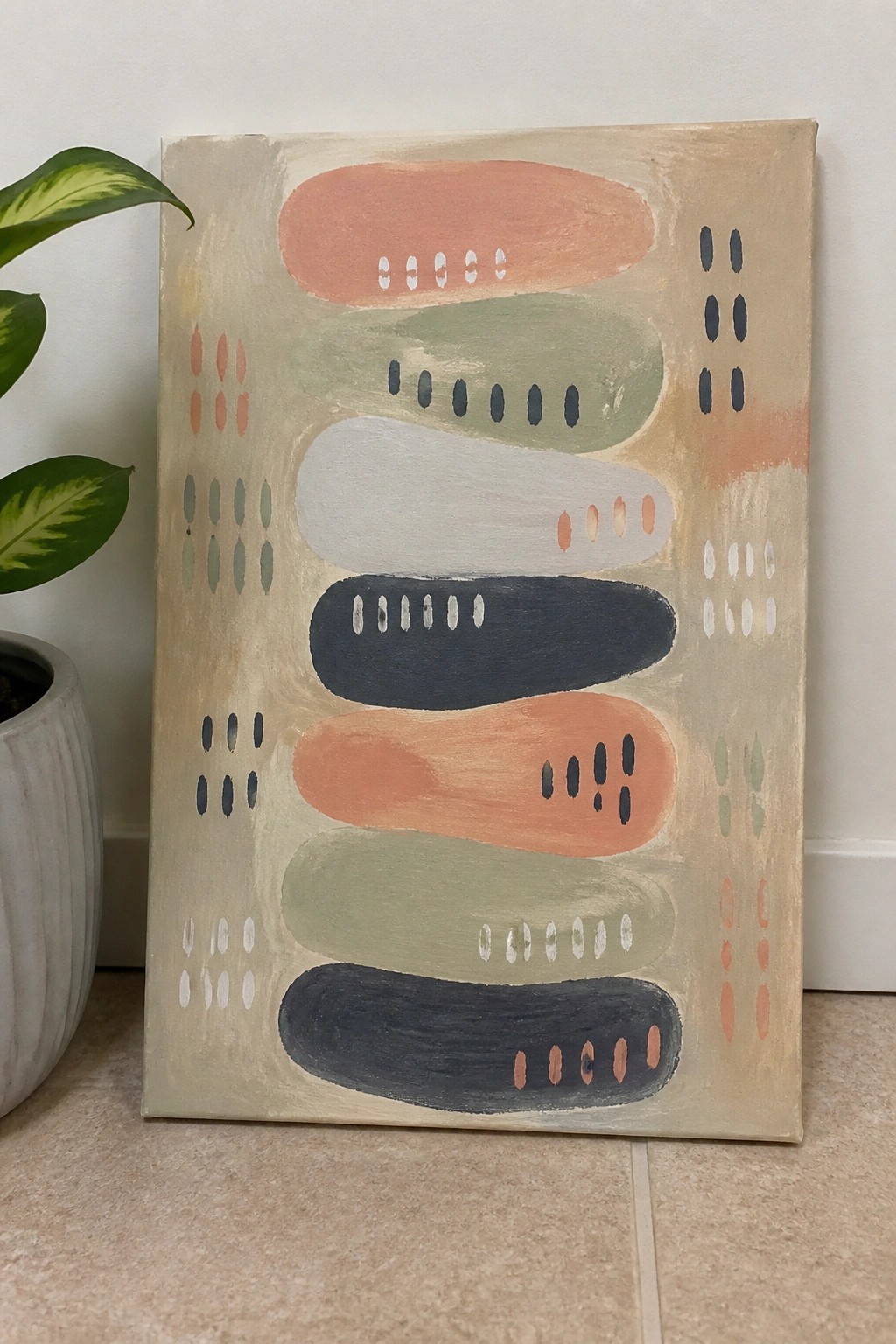 An acrylic painting on canvas with stacked rounded shapes in peach, green, gray, and black on a beige background, plus dotted patterns along both sides.