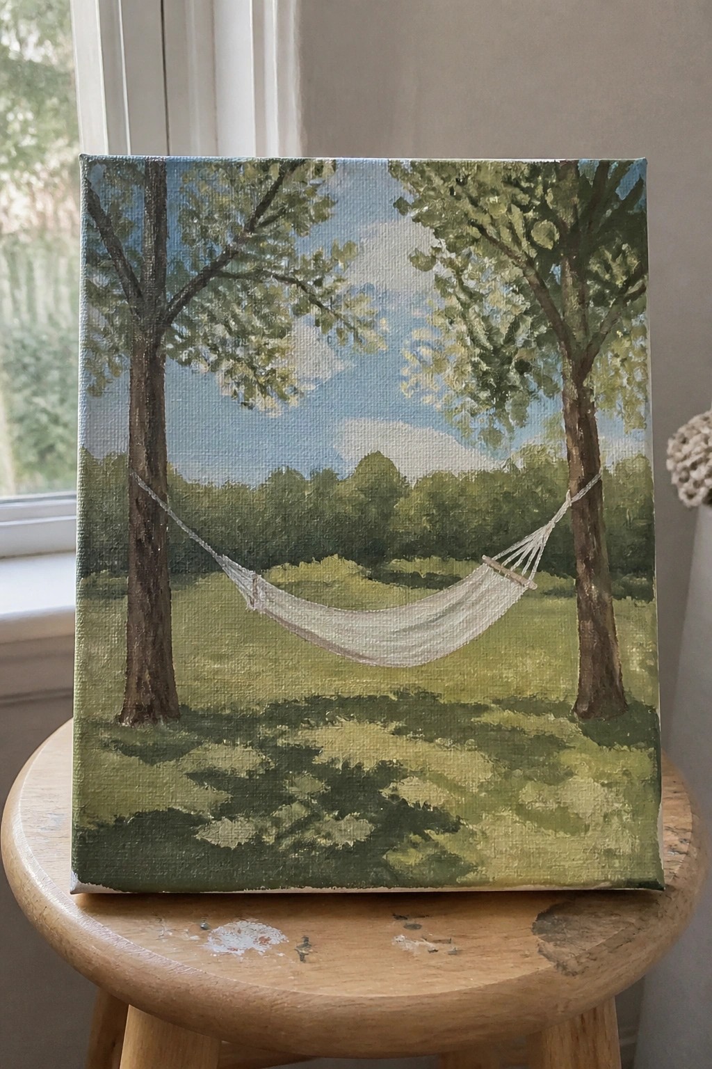 Canvas painting of white hammock between trees in green field on wooden stool