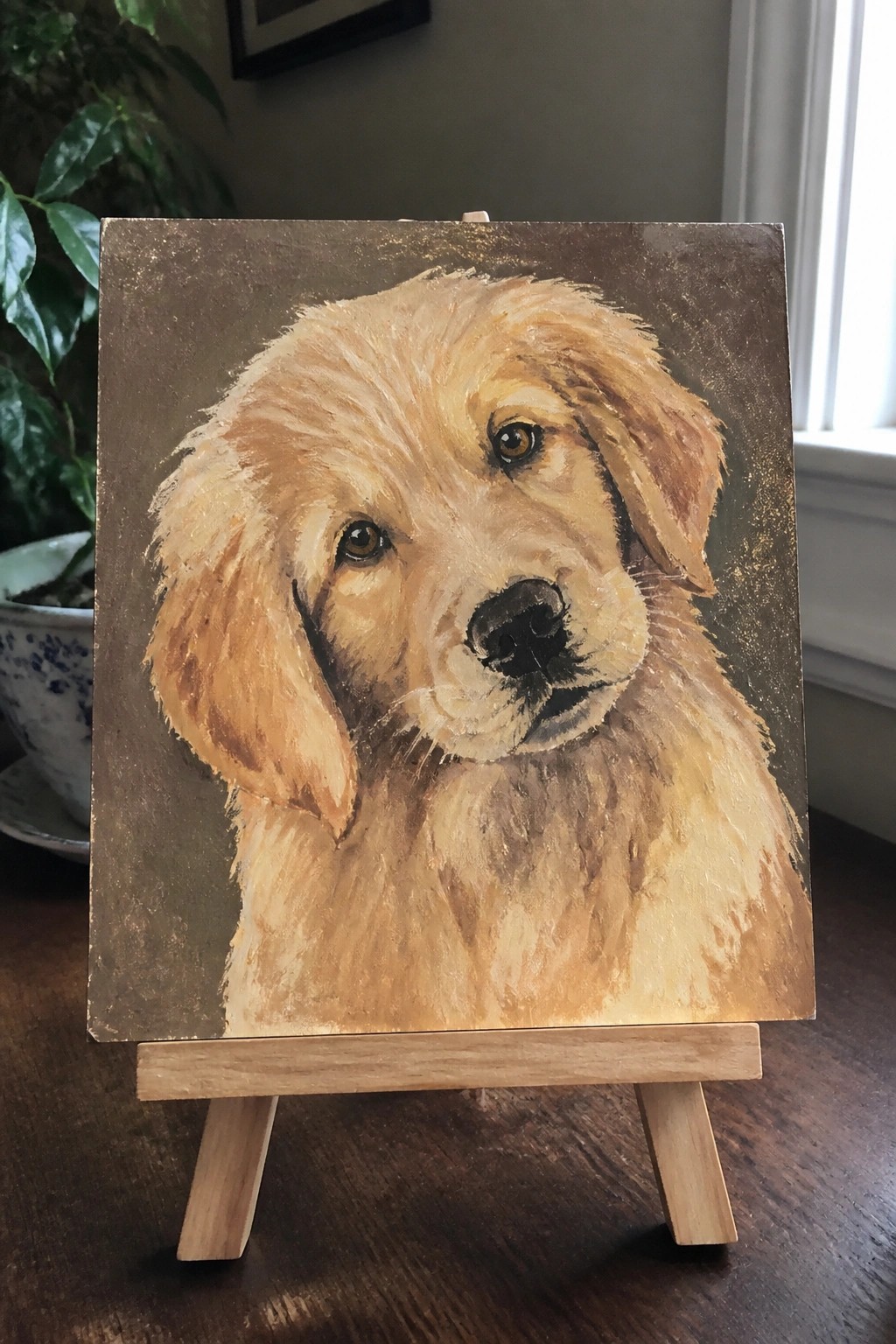 Golden retriever puppy portrait painted on canvas atop small wooden easel.