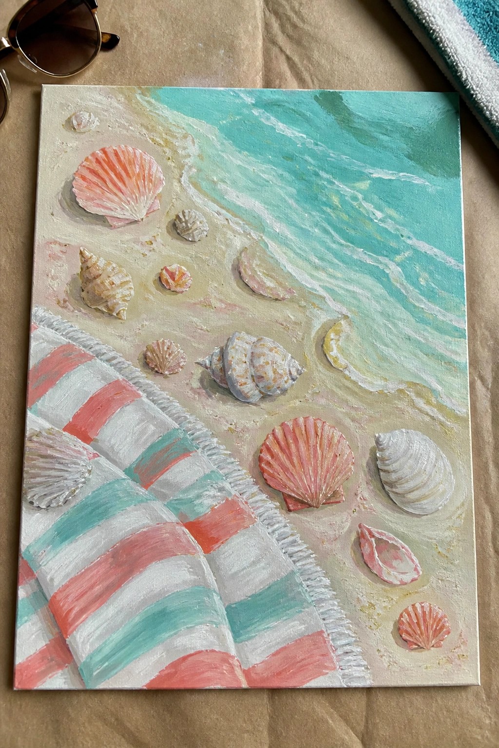 An acrylic painting of seashells scattered on sand beside a striped beach towel with turquoise waves in the background.