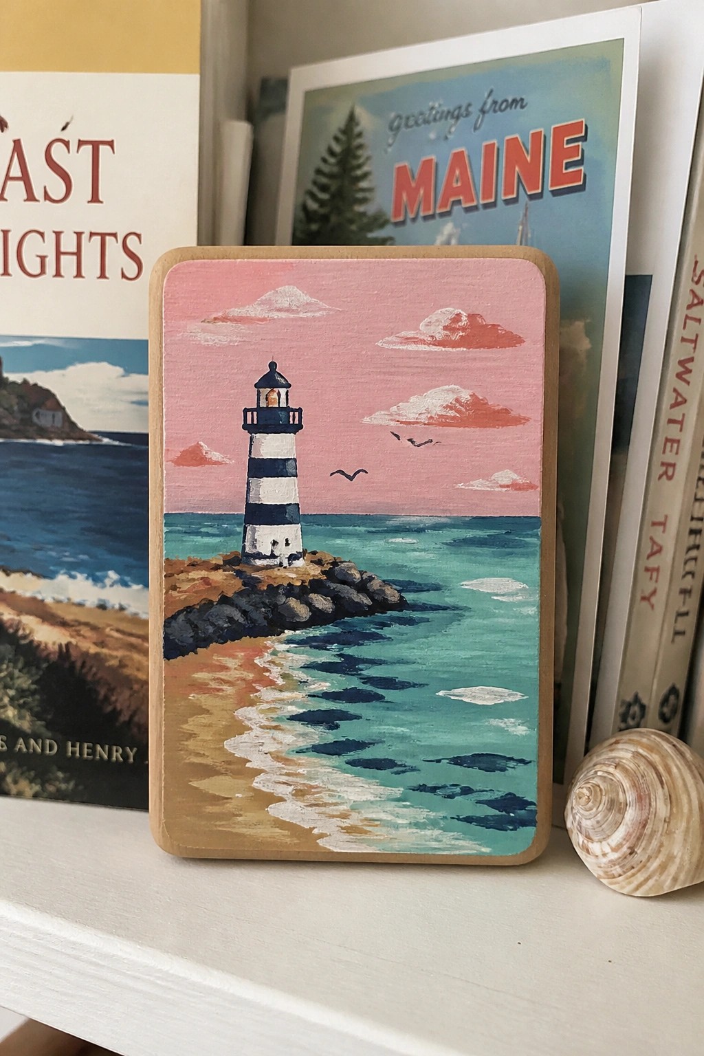 Painted wooden block of striped lighthouse on rocky shore by turquoise sea under pink sky.