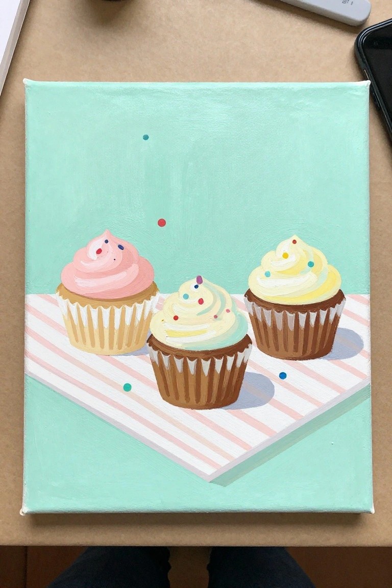 Three cupcakes with pink, yellow, and mint frosting on striped cloth against green background