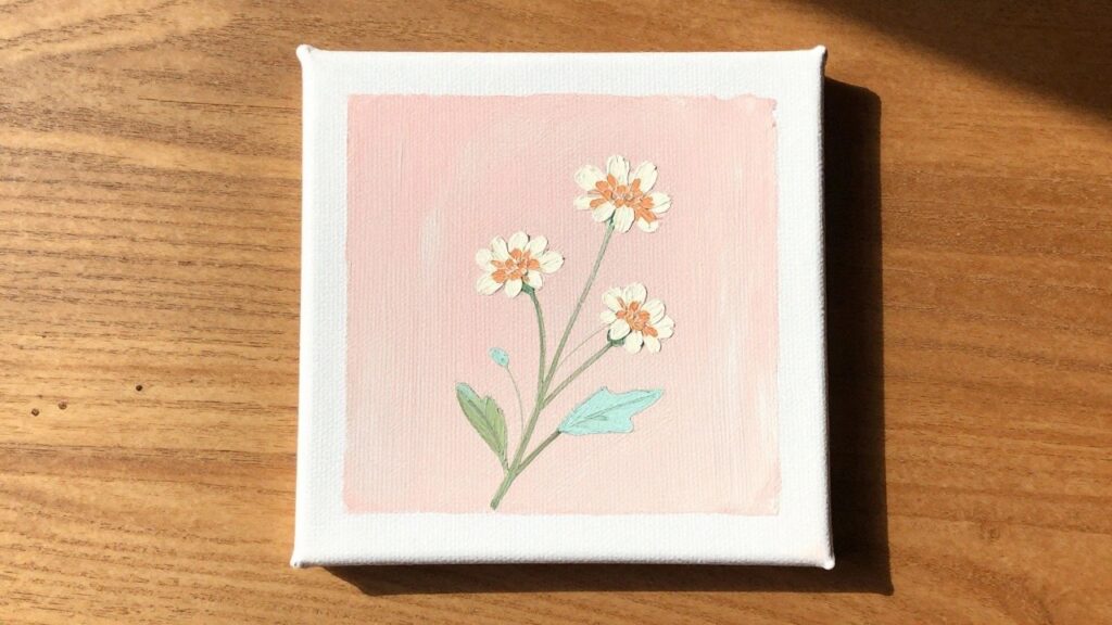 Pink canvas with textured white, peach, and teal flowers on wooden surface