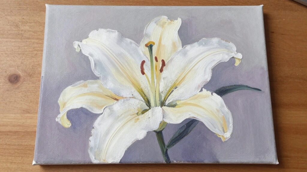 White lily painting with yellow accents on light purple canvas atop wooden table