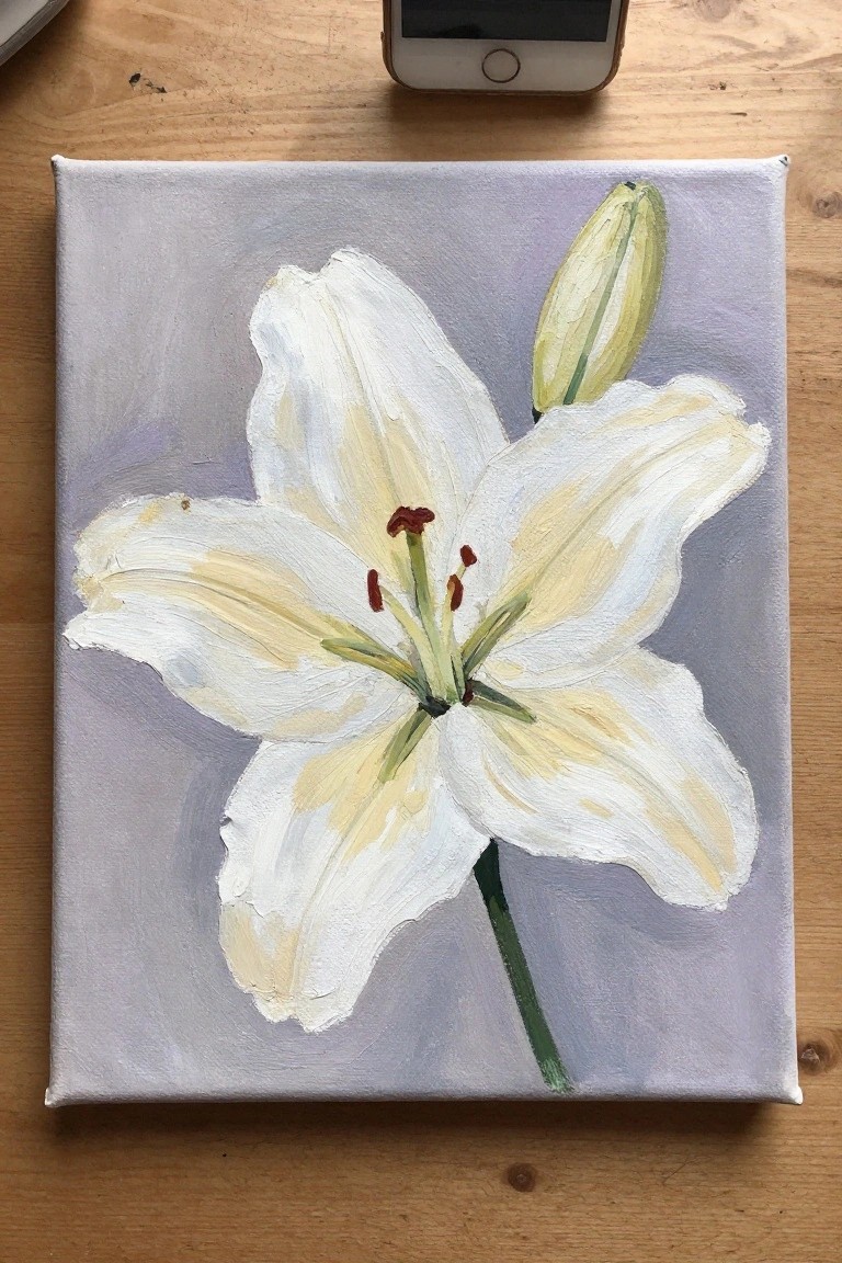 White lily painting with yellow accents on light purple canvas atop wooden table