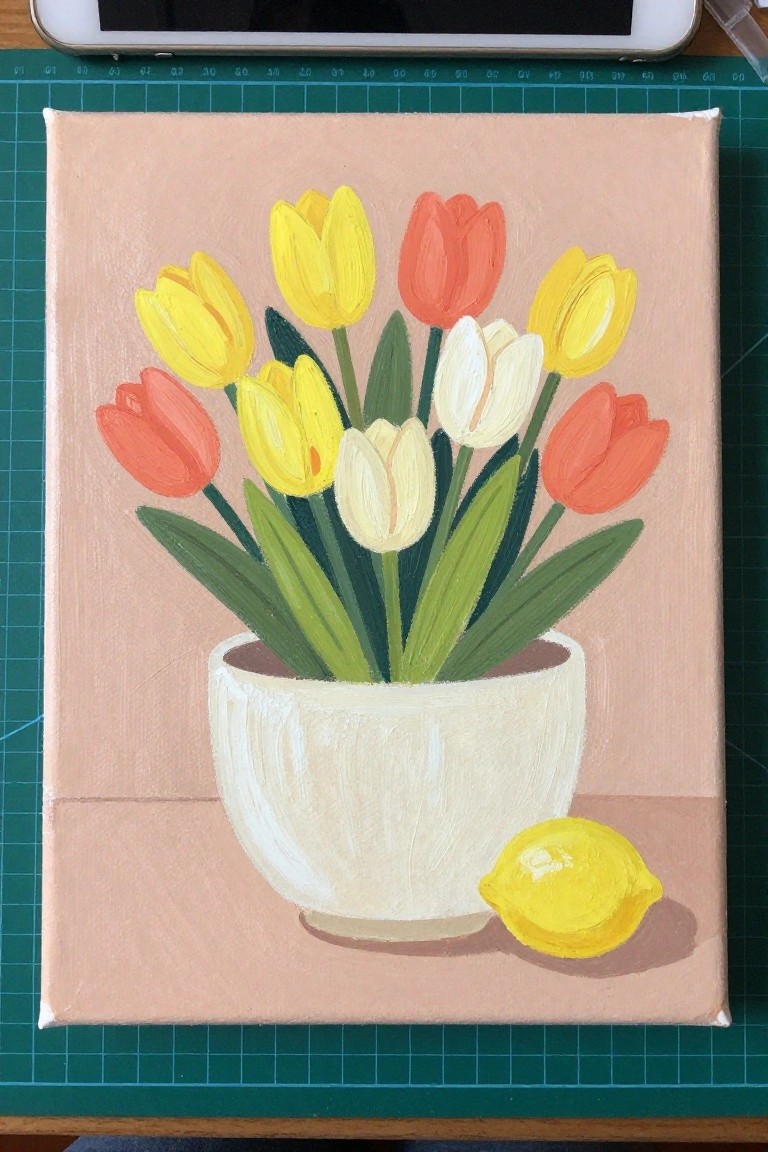 Colorful tulips in a white bowl beside a yellow lemon on pink background