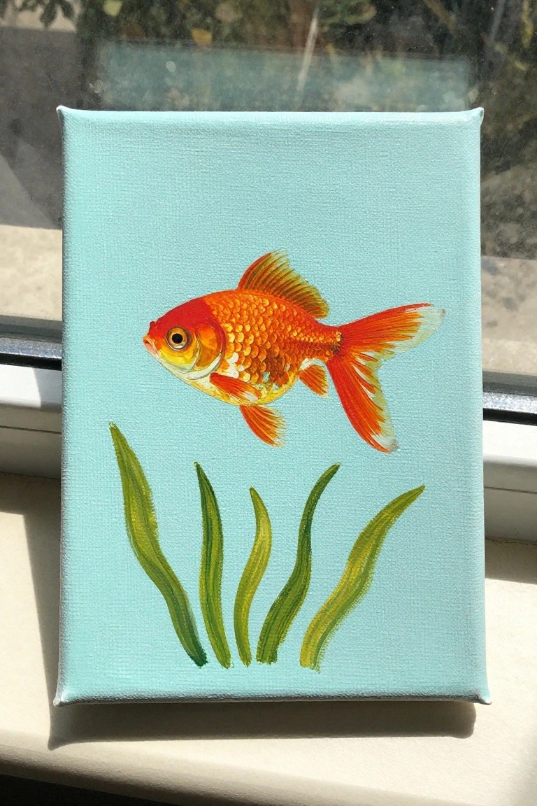 A small canvas painting of an orange goldfish above green plant strokes on a light blue background.