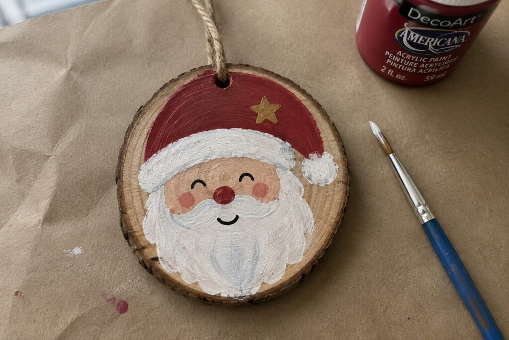 Painted Santa ornament on wood slice with red hat, gold star, white beard