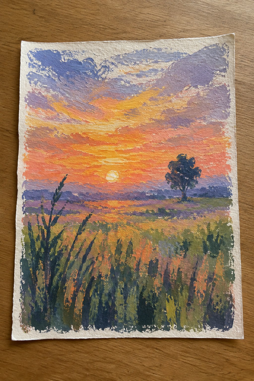 Vibrant sunset painting over golden field with lone silhouetted tree and streaked colorful clouds