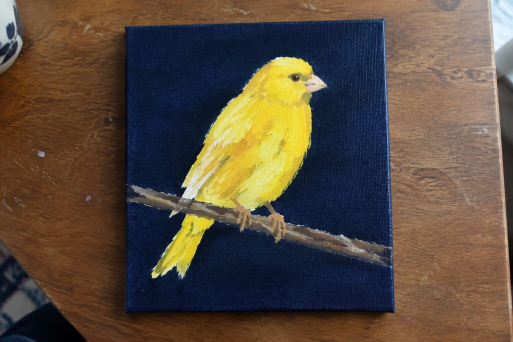 16 Bright Yellow Bird Acrylic Painting Ideas With High-Contrast Backgrounds Yellow canary perched on branch against dark blue canvas on wooden table