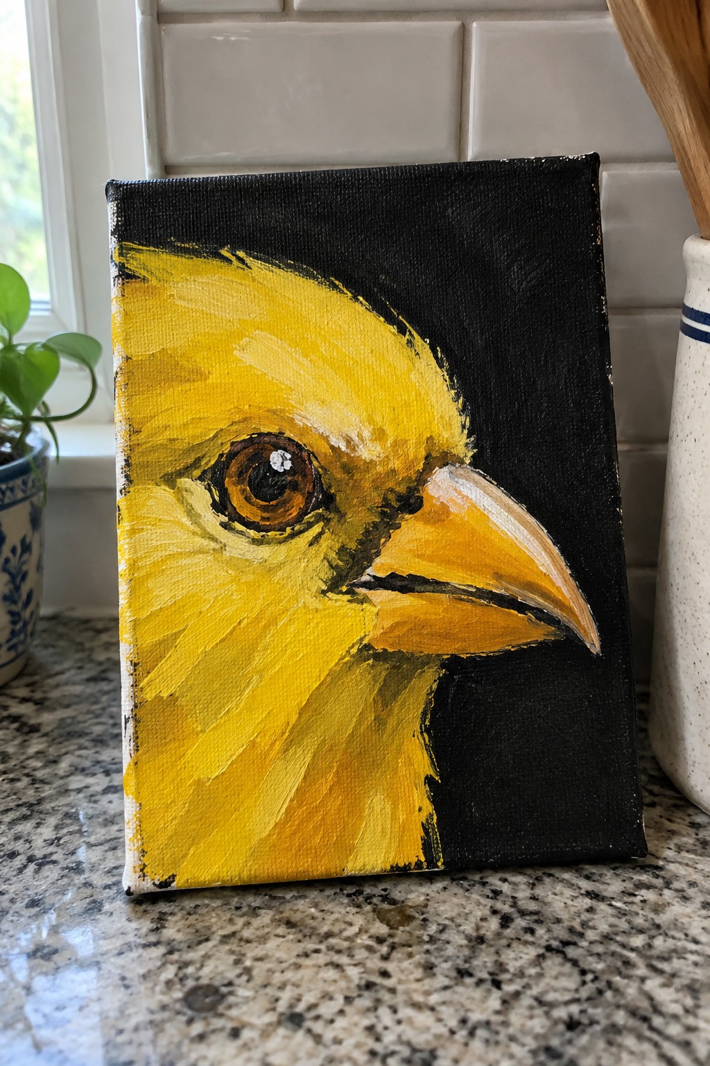 Bright yellow bird painting with large brown eye and orange beak on black canvas.