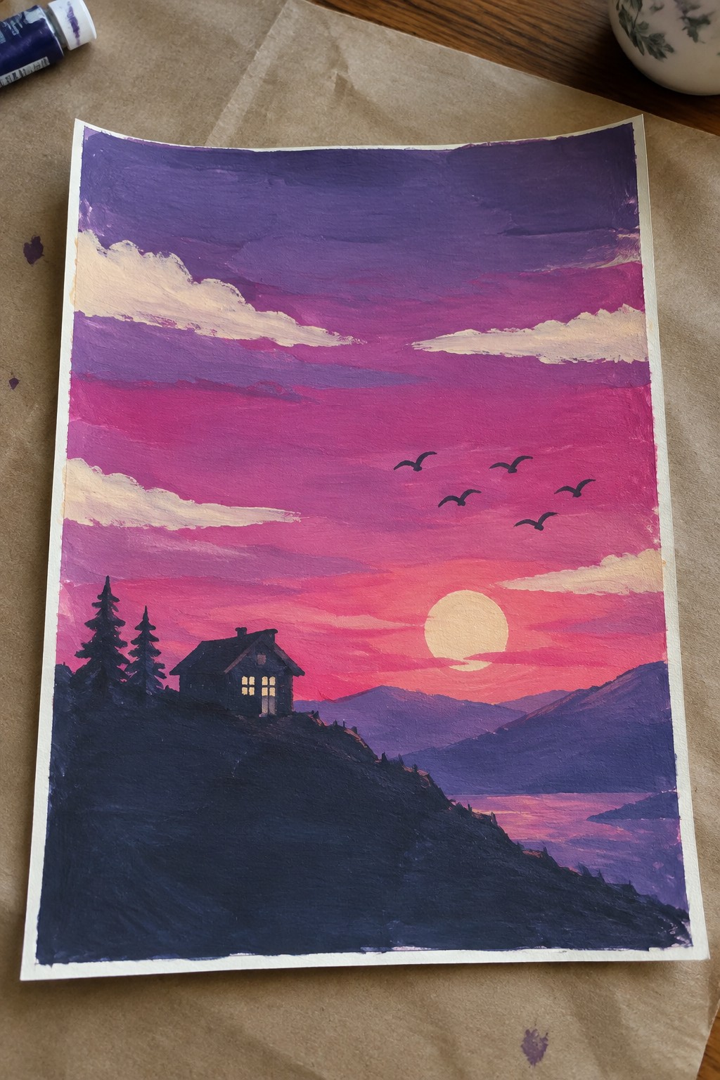 Vivid painting of dark cabin on hill with lit windows under pink-purple sunset sky and birds.