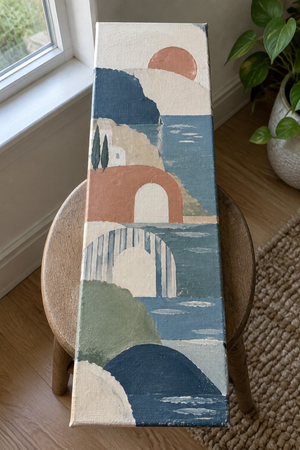 Abstract landscape painting with arches, sun, and hills on canvas atop wooden stool.