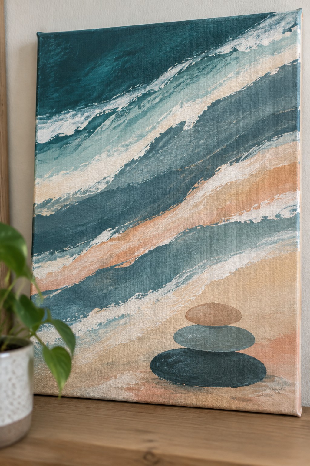 Abstract painting of teal waves above stacked stones on a peach beach canvas