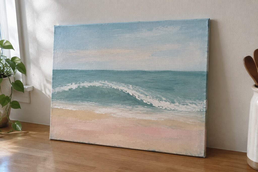 Canvas beach painting with blue wave on granite counter beside potted plant