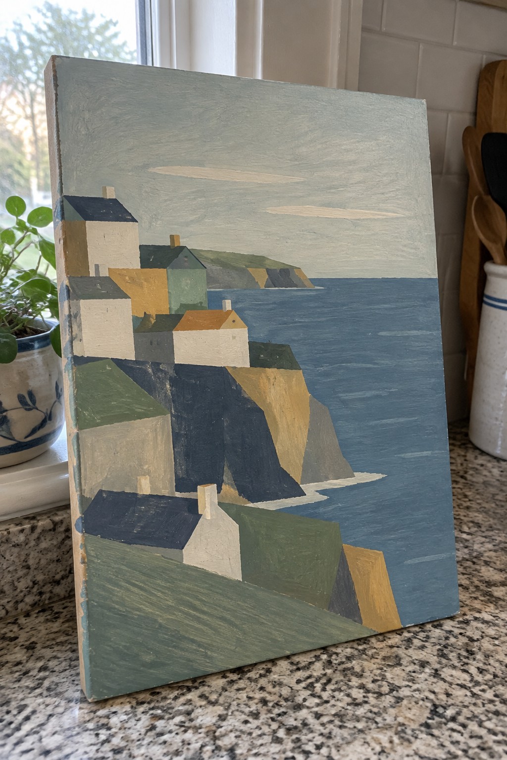 Acrylic painting of simplified geometric buildings on layered cliffs beside blue water with muted earth tones and flat shapes.